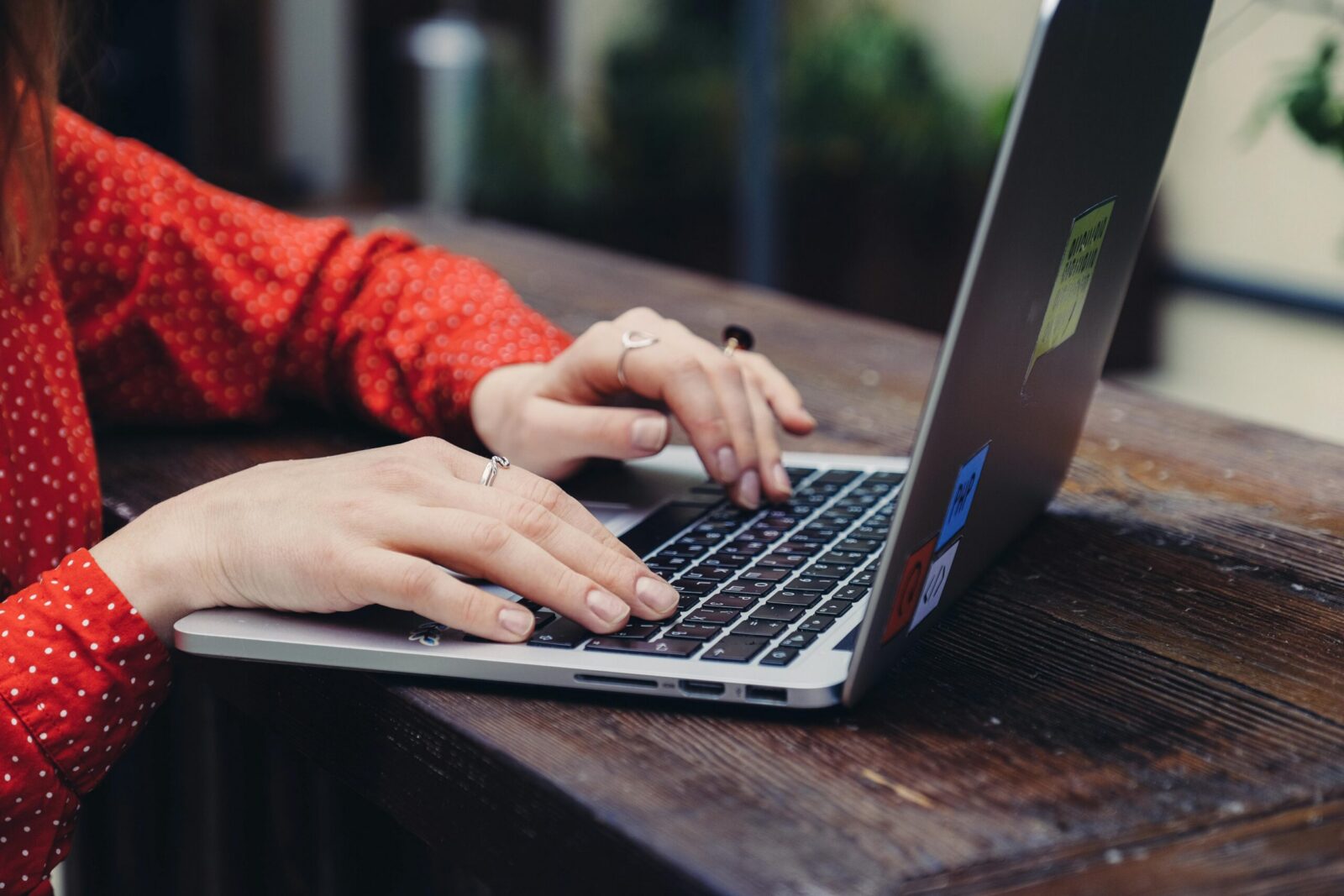 Close-up of hands typing on a laptop placed on a wooden table outdoors.